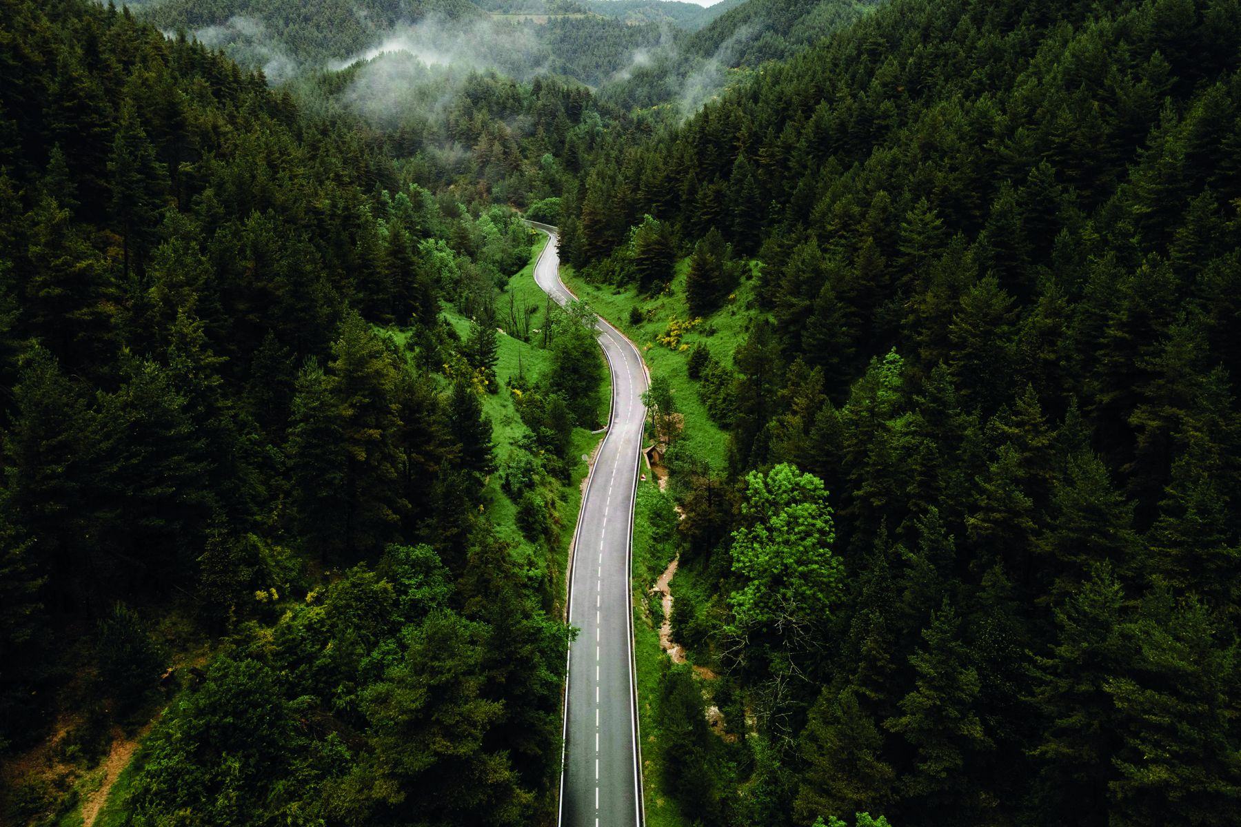 An aerial view of an empty road winding through misty forested hills